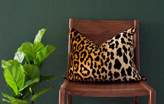 a chair with a leopard pillow and a plant on the side