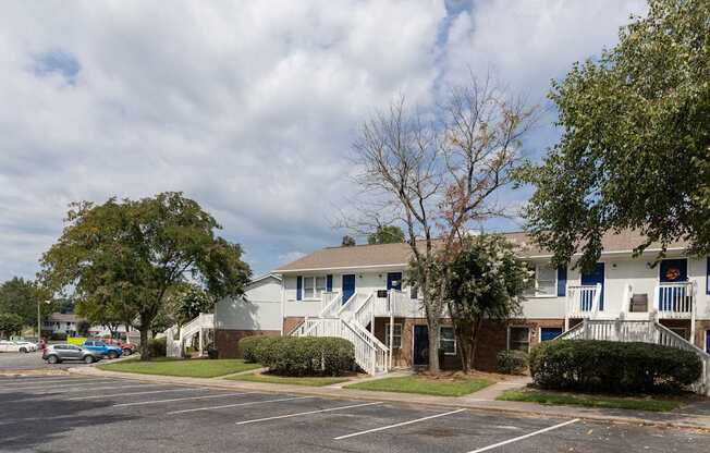 A parking lot in front of a two-story building with a blue sky and clouds in the background.