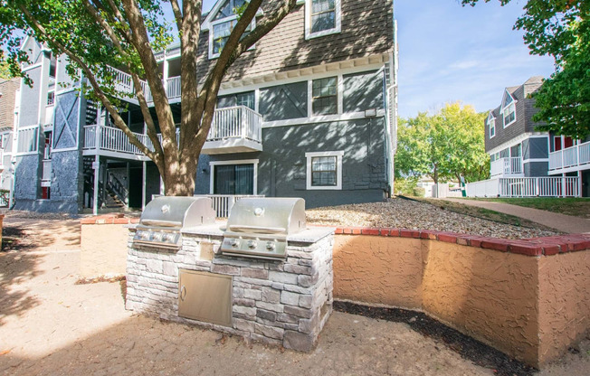 an outdoor kitchen with a grill and a tree in front of an apartment building