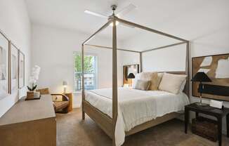 A bedroom with a four poster bed and a table with a lamp on it.