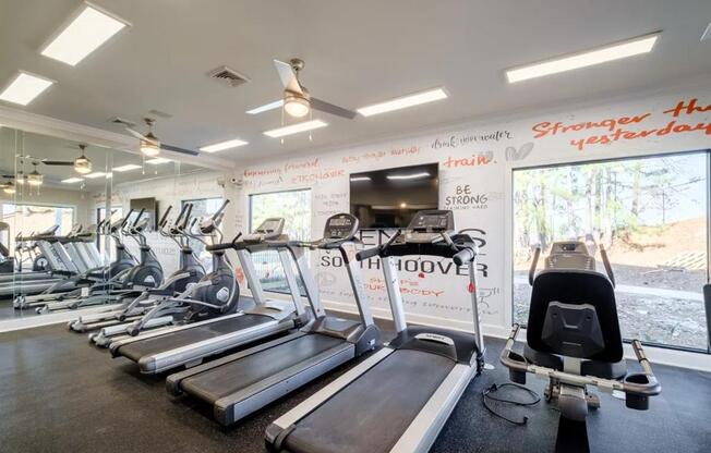 a gym with cardio equipment and a wall of windows