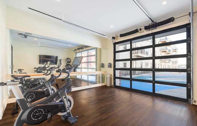 A room with a row of stationary bikes and a view of a pool outside.