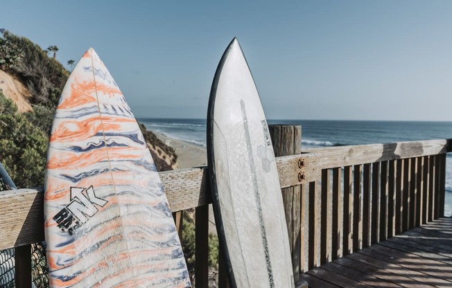 two surfboards leaning against a fence next to the beach