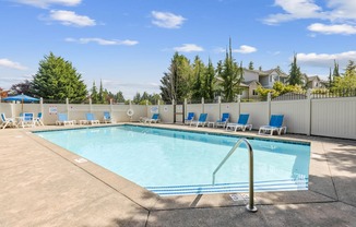 A large swimming pool surrounded by a white fence and blue lounge chairs at Abbey Rowe Apartments in Olympia, WA