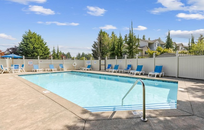 A large swimming pool surrounded by a white fence and blue lounge chairs at Abbey Rowe Apartments in Olympia, WA
