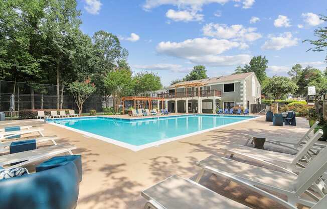 A large swimming pool with sun loungers and a building in the background.