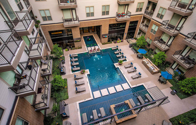 A large swimming pool surrounded by lounge chairs and balconies of apartment buildings.