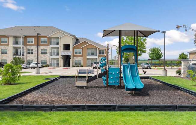 A playground with a blue slide and a brown building in the background.