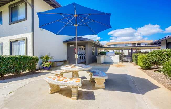 a patio with a blue umbrella and two tables with umbrellas