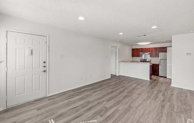 an empty living room and kitchen with white walls and wood flooring