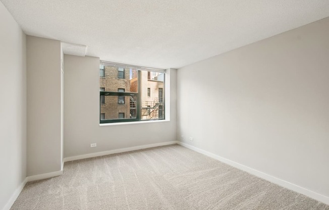 A room with a carpeted floor and a window showing a view of buildings outside.