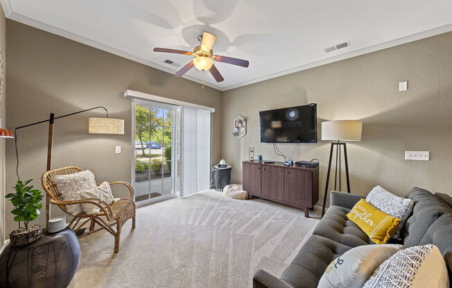 large living room with sliding glass doors to deck, illuminated ceiling fan, and model decor