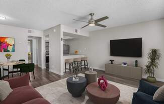 A living room with a red couch, a grey ottoman, and a television on the wall.