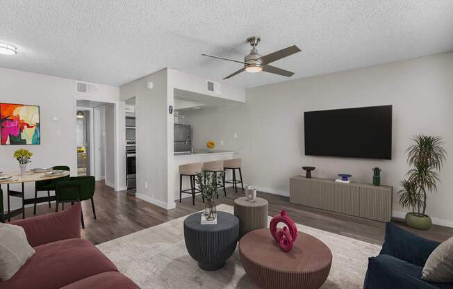 A living room with a red couch, a grey ottoman, and a television on the wall.