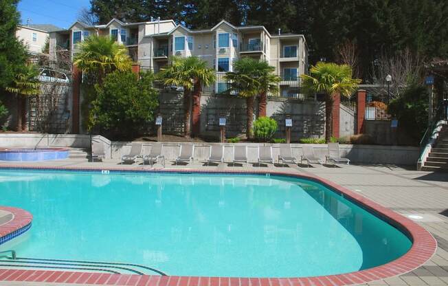 A swimming pool surrounded by a stone wall and palm trees at Wilsonville Summit Apartments, Wilsonville 