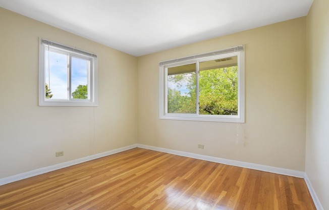 an empty room with two windows and wood floors