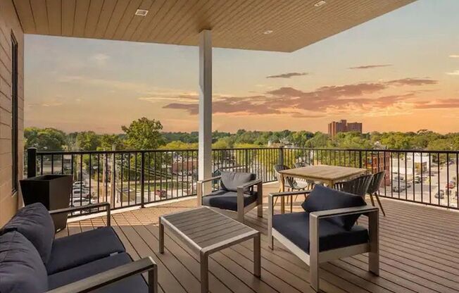 A balcony with a table and chairs overlooking a cityscape at sunset.