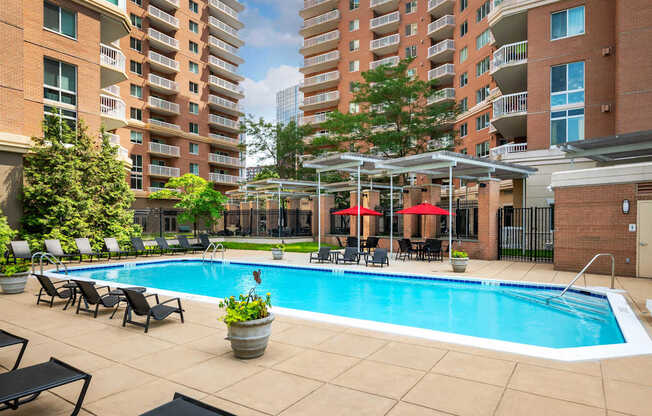 A large swimming pool surrounded by lounge chairs and umbrellas in a courtyard.