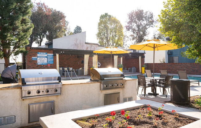 A patio with a grill and chairs under yellow umbrellas.