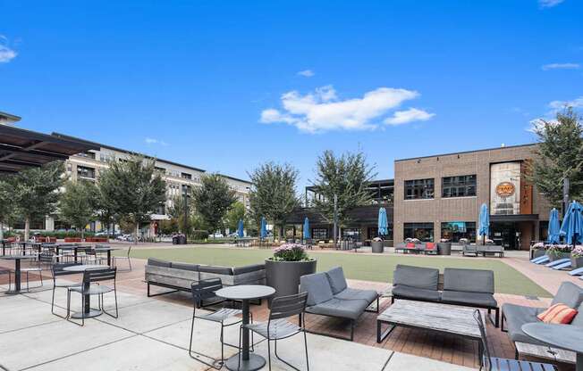 a patio area with tables and chairs and a lawn in front of a building