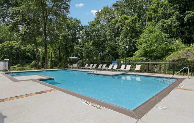 A pool with lounge chairs surrounded by lush trees at Gwinnett Square Apartments in Duluth, GA