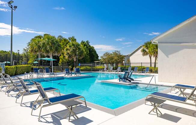 A pool with blue water and lounge chairs around it.