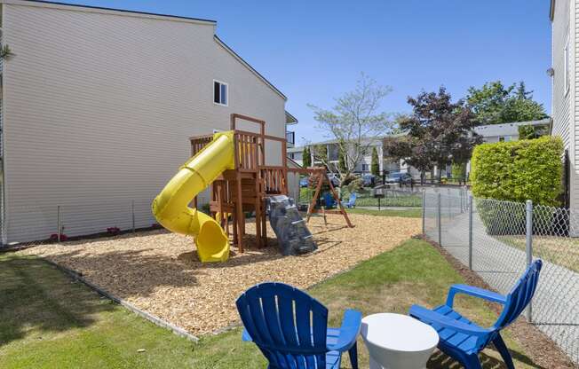 Property playground with a yellow slide in the middle with blue chairs and a table for supervision at Park Edmonds Apartment Homes, Edmonds