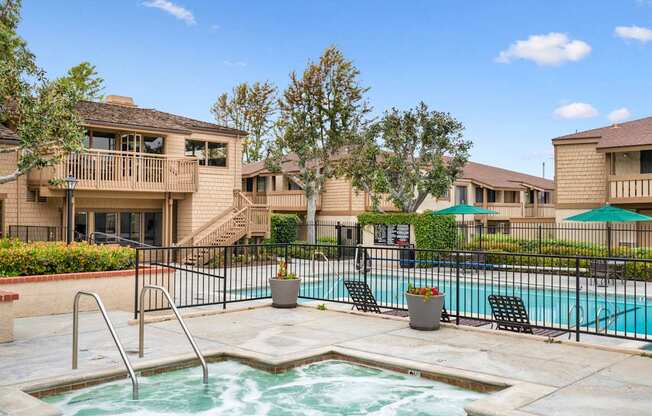 A pool with a hot tub in the middle of a patio surrounded by chairs and trees.