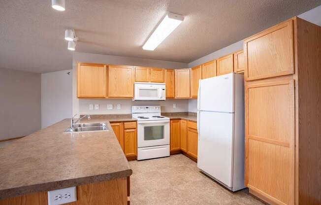 A kitchen with wooden cabinets and white appliances. Fargo, ND East Bridge Apartments