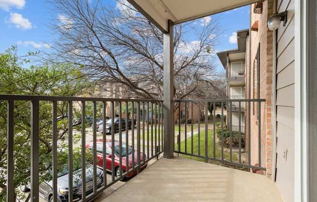 A balcony with a black railing and a view of a parking lot and trees.