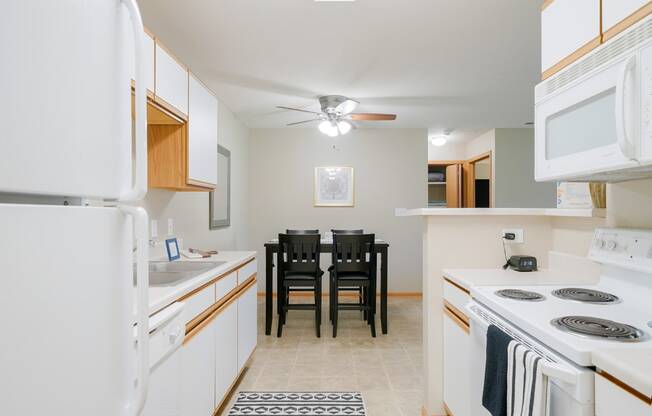 a kitchen with white appliances and a dining room table with chairs in the back