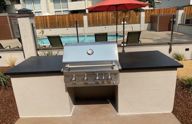 a gas grill on a patio next to a pool