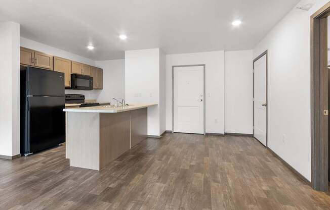 A kitchen with a black refrigerator and wooden floors.