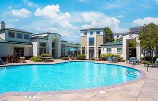 A swimming pool surrounded by a patio with chairs and a building in the background.