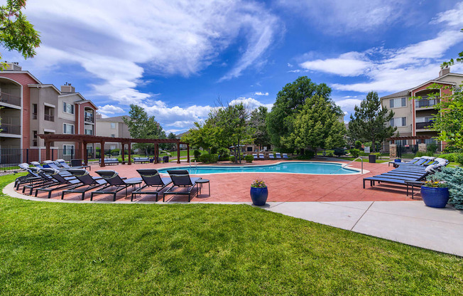 A swimming pool surrounded by lawn chairs and trees.