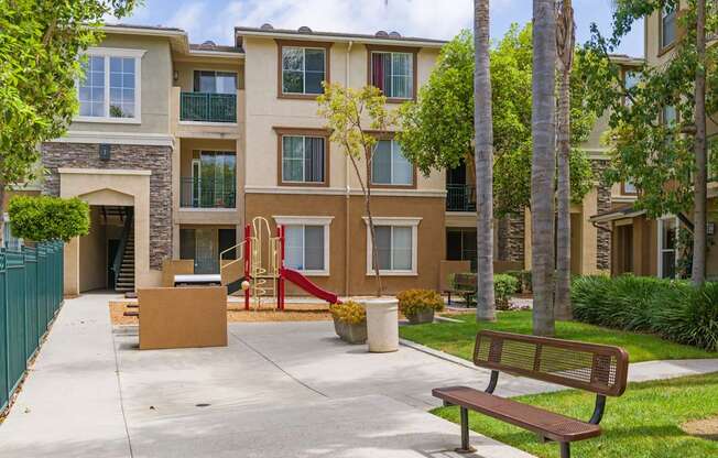A brown bench sits on a sidewalk in front of a building.