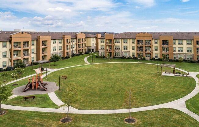 a park with a large grassy area and a playground in front of an apartment building