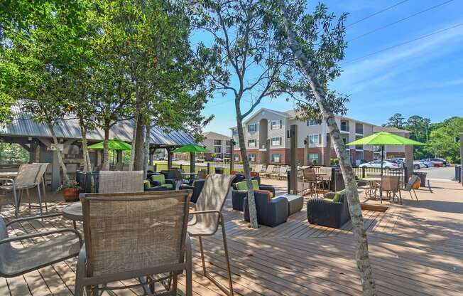 a patio with tables chairs and umbrellas and a building in the background at Lagniappe of Biloxi Apartment Homes, Biloxi, MS