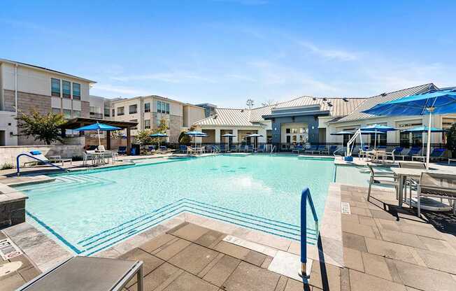 A large swimming pool surrounded by a tiled patio and lounge chairs.