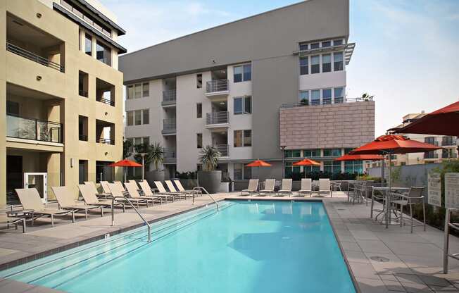 a swimming pool with chaise lounge chairs and umbrellas in front of a building