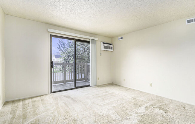 an empty living room with a sliding glass door to a balcony