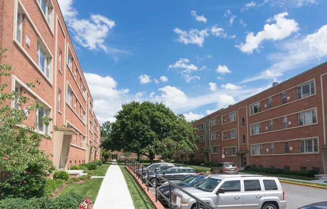 A sunny day at a brick apartment complex with cars parked on the street.