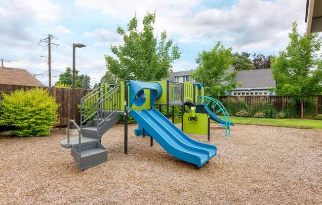 a playground with a blue slide and chairs in a yard