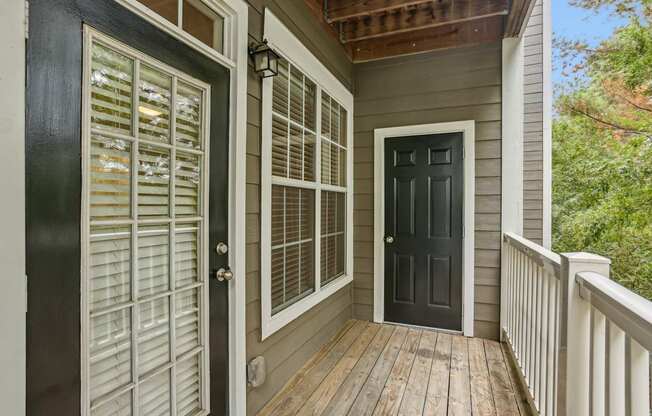 A wooden deck with a black door and a window with white shutters.