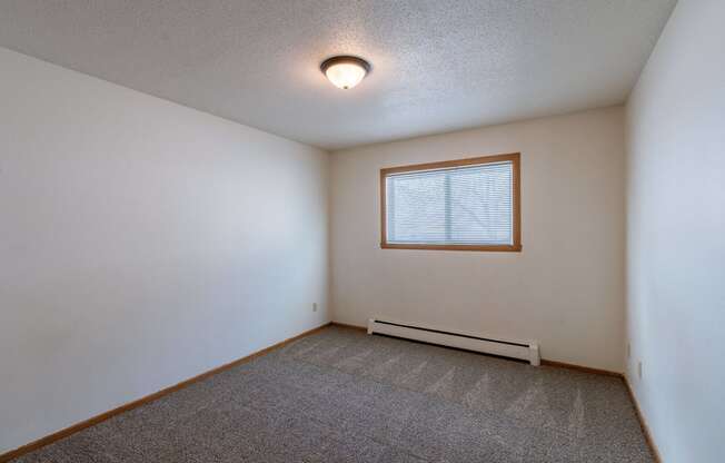 a bedroom with white walls and a window. Fargo, ND Schrock Apartments