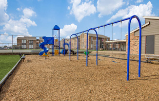 Pet-Friendly Apartments in Fort Worth TX - Monarch Pass - Playground with Swings, Slide Tower, and View of Apartment Buildings