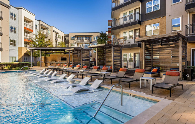 A swimming pool with lounge chairs and apartment buildings in the background.
