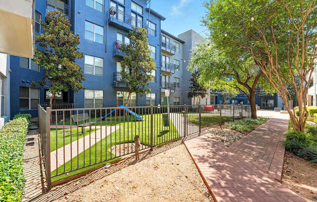 A tree-lined walkway leads to a gated courtyard with a playground.