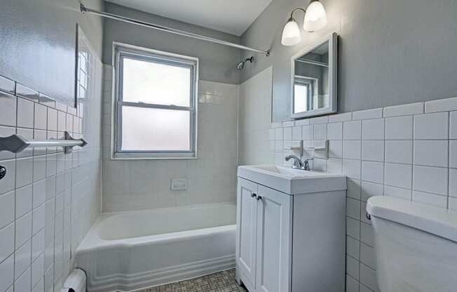 a bathroom with white tiled walls and floors and a white bathtub with a shower curtain