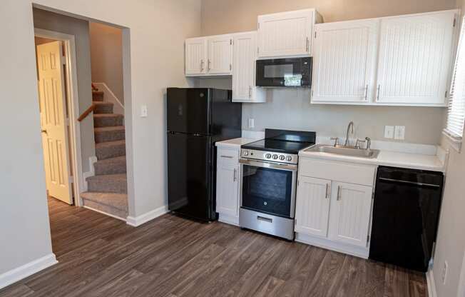 Spacious kitchen with white cabinetry,  black energy efficient appliances and plank style flooring